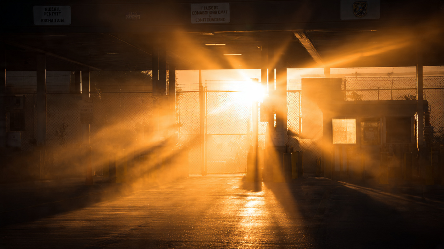 The sun blazing through an empty customs border checkpoint, golden light streaming past inspection booths